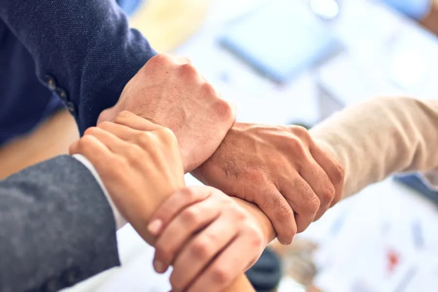 Mãos de uma equipe unidas sobre a mesa de reunião